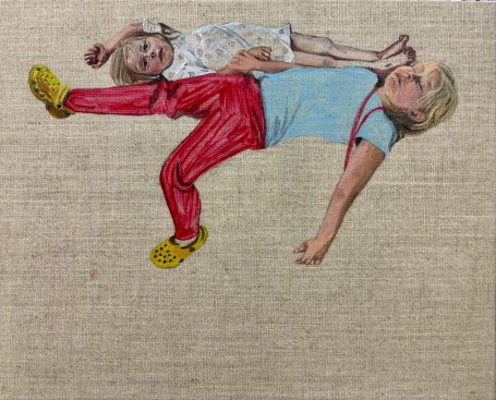 Two children playfully lying on a textured surface, one resting on the other's back.