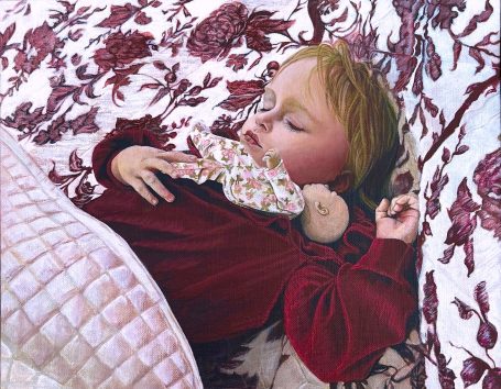 A young girl sleeps peacefully with a doll on a patterned blanket.