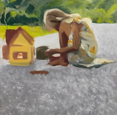 Child playing on the ground near a small house, engaged in creative activities.