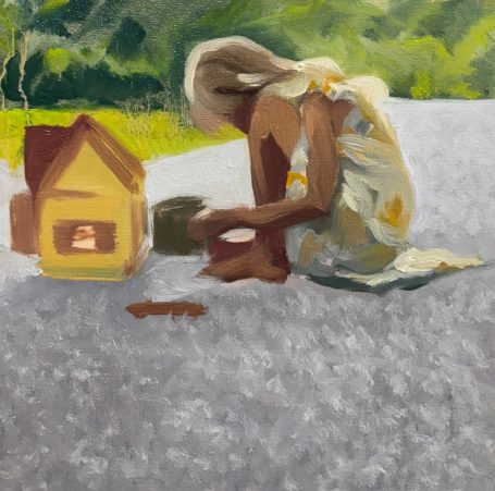 Child playing on the ground near a small house, engaged in creative activities.